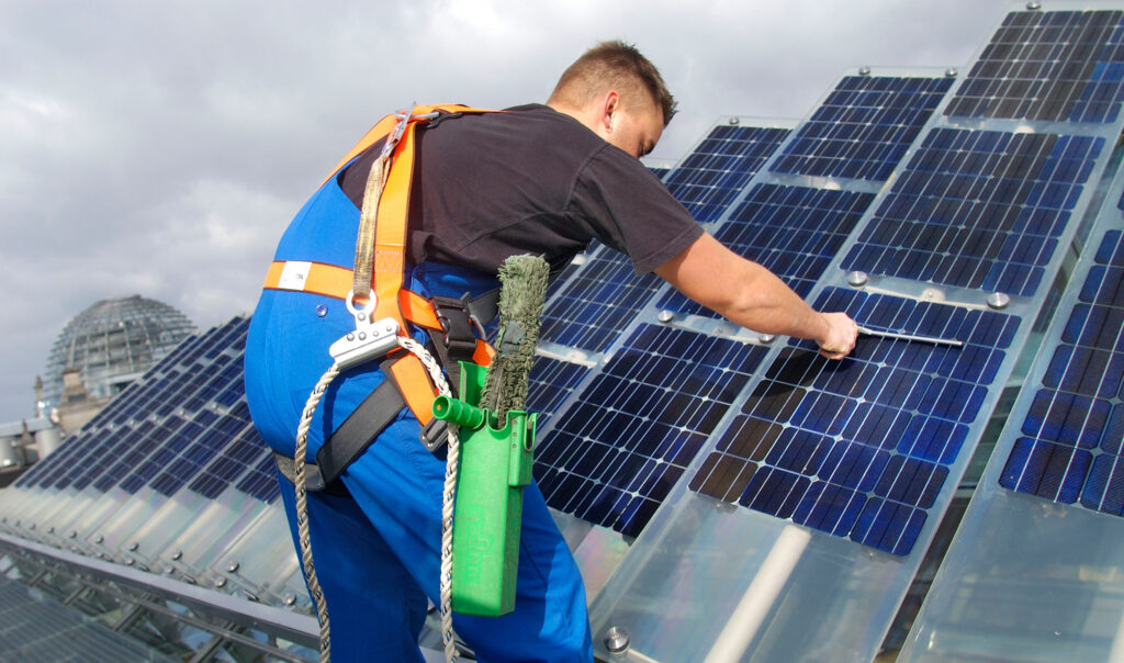Fachkraft reinigt eine Photovoltaikanlage auf dem Dach mit Spezialwerkzeug im Rahmen der professionellen Solarreinigung